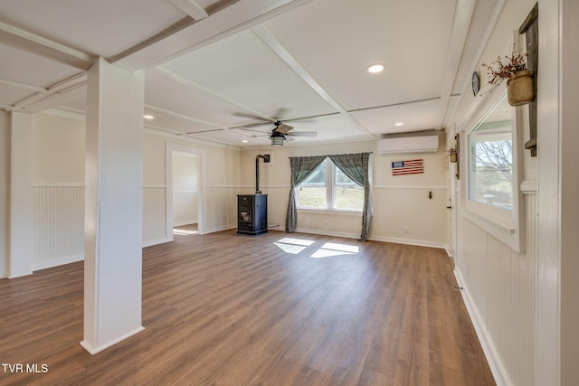 unfurnished living room with ceiling fan, a wall mounted air conditioner, wainscoting, a wood stove, and wood finished floors