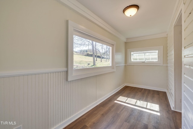 spare room featuring dark wood finished floors, a wainscoted wall, baseboards, and ornamental molding