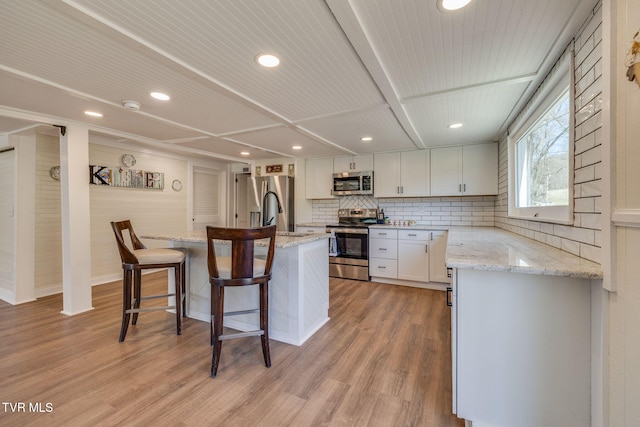 kitchen featuring appliances with stainless steel finishes, a kitchen bar, light wood-style floors, and a kitchen island with sink