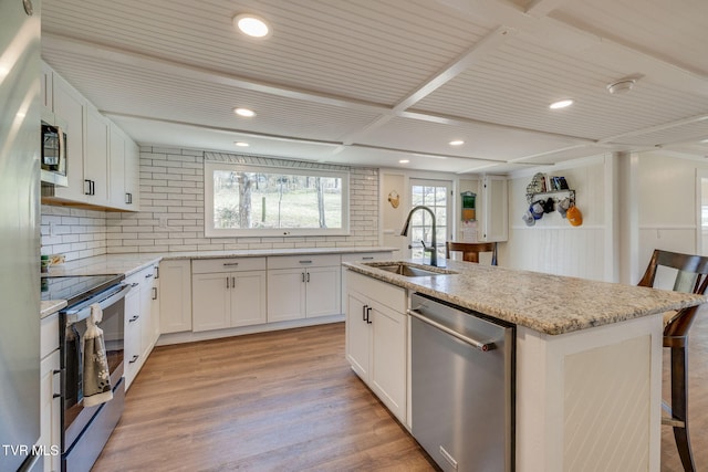 kitchen featuring light stone countertops, a center island with sink, light wood-style flooring, appliances with stainless steel finishes, and a sink