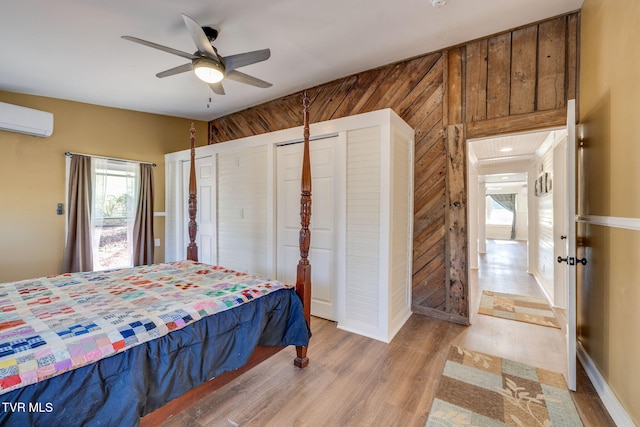 bedroom with light wood-type flooring, wood walls, a ceiling fan, and a wall unit AC