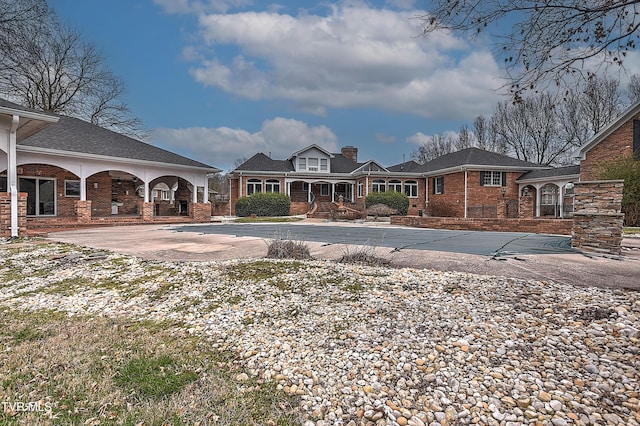 rear view of house with brick siding, curved driveway, and a chimney