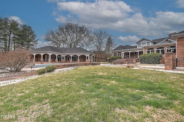 back of property featuring covered porch, a lawn, and brick siding