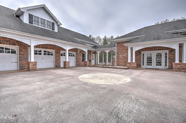 exterior space featuring concrete driveway, an attached garage, french doors, and brick siding