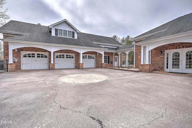 view of front facade with brick siding, concrete driveway, roof with shingles, french doors, and an attached garage