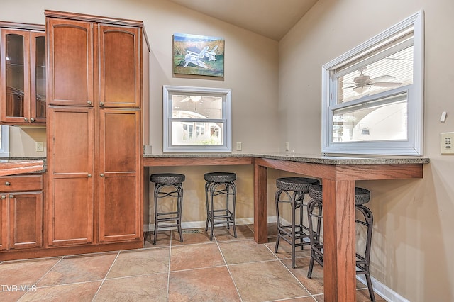 kitchen featuring a breakfast bar, light tile patterned flooring, brown cabinetry, and vaulted ceiling