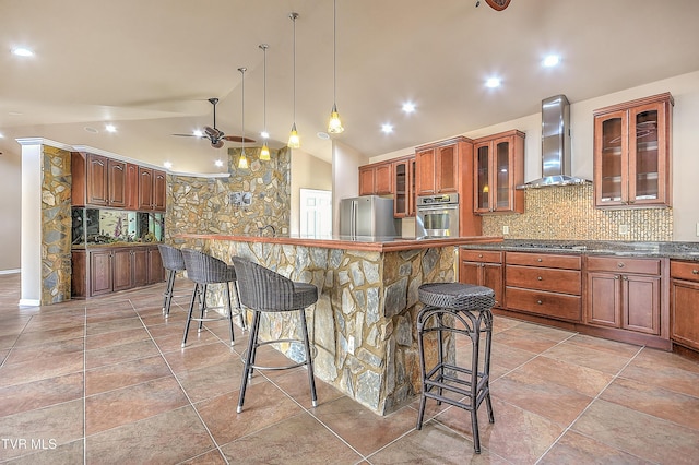 kitchen featuring a breakfast bar, lofted ceiling, stainless steel appliances, wall chimney exhaust hood, and backsplash