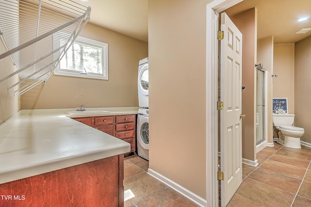 interior space featuring toilet, a stall shower, a sink, stacked washing maching and dryer, and tile patterned flooring