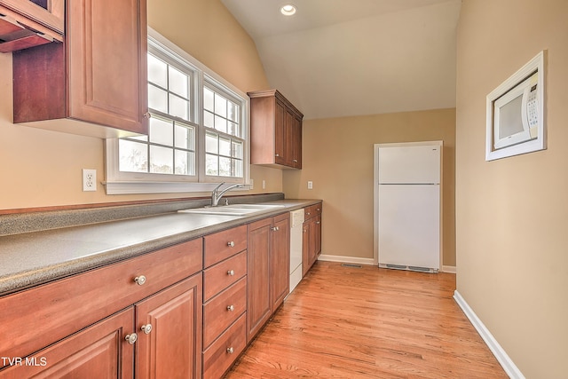 kitchen with white appliances, baseboards, light wood-style flooring, a sink, and vaulted ceiling