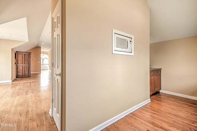 corridor with light wood-type flooring, lofted ceiling, and baseboards