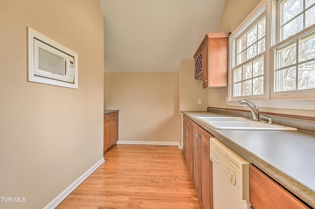 kitchen with a sink, light wood-style floors, brown cabinetry, baseboards, and dishwasher