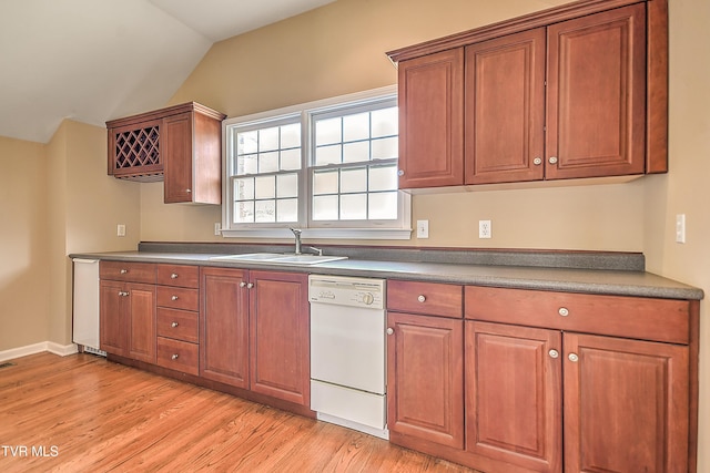 kitchen featuring light wood finished floors, a sink, brown cabinetry, white dishwasher, and vaulted ceiling