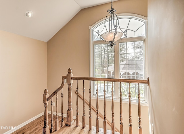 staircase with baseboards, a notable chandelier, wood finished floors, and vaulted ceiling