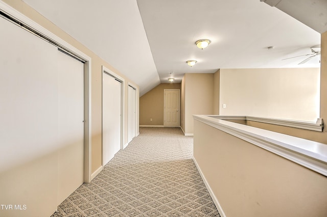 hall featuring lofted ceiling, light colored carpet, and baseboards