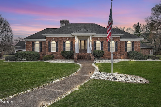 view of front of house with brick siding, a chimney, and a front lawn