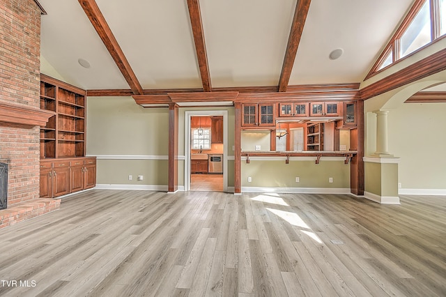 unfurnished living room with light wood finished floors, beam ceiling, arched walkways, high vaulted ceiling, and ornate columns