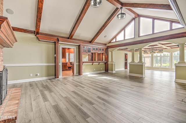 unfurnished living room with ornate columns, high vaulted ceiling, beam ceiling, light wood-style flooring, and arched walkways