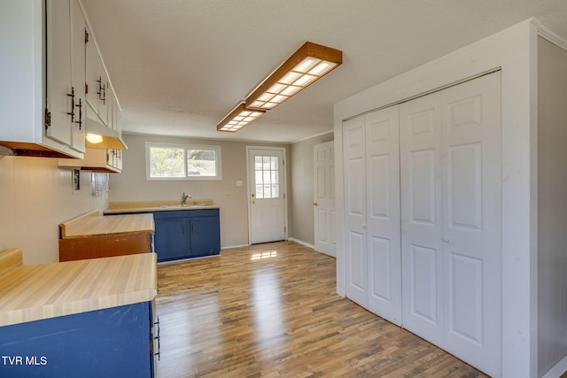 kitchen with blue cabinetry, a sink, wood finished floors, white cabinets, and butcher block counters