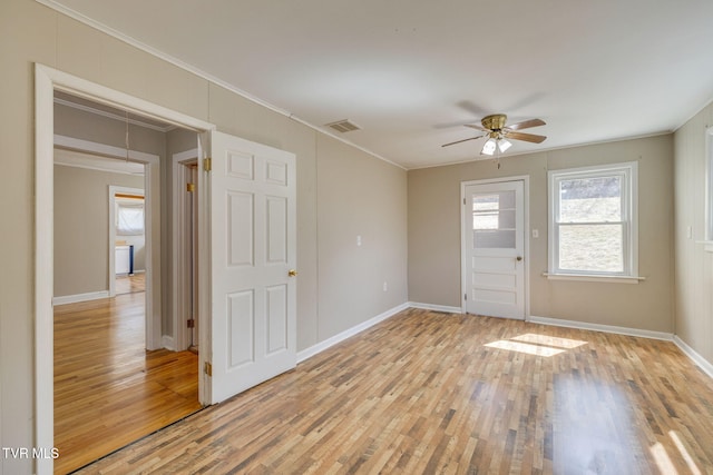 spare room featuring light wood finished floors, visible vents, baseboards, ornamental molding, and a ceiling fan