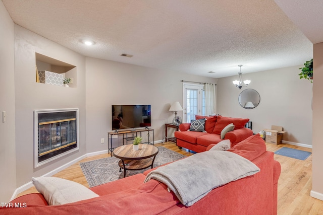 living room with visible vents, baseboards, wood finished floors, a glass covered fireplace, and a textured ceiling