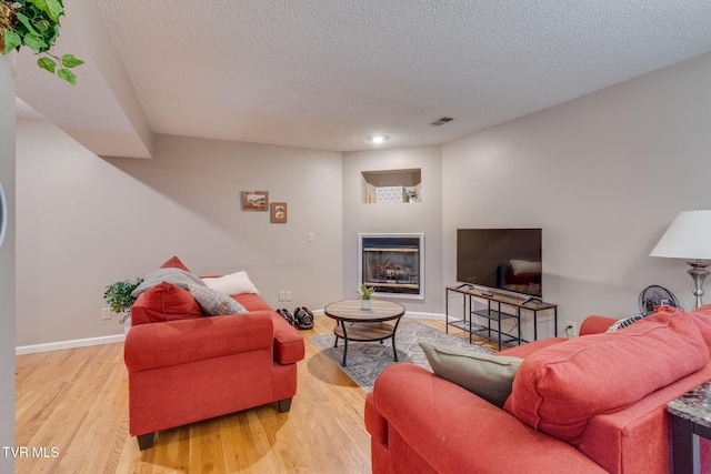 living room featuring a glass covered fireplace, visible vents, baseboards, and wood finished floors