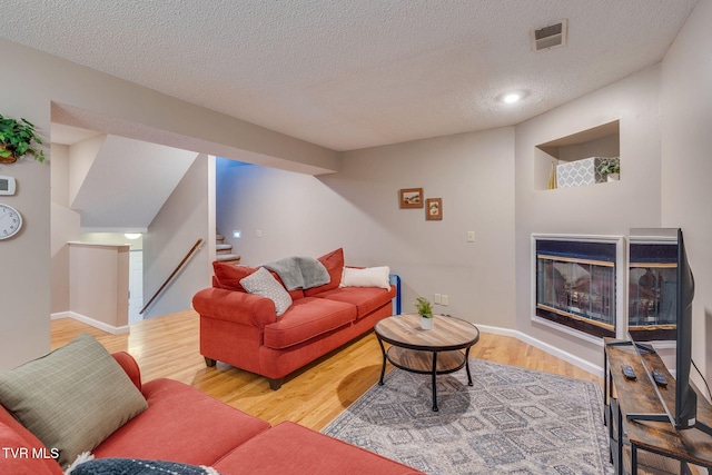 living room featuring stairway, wood finished floors, visible vents, a multi sided fireplace, and a textured ceiling