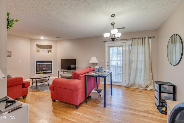 living area with baseboards, visible vents, light wood finished floors, a textured ceiling, and a glass covered fireplace