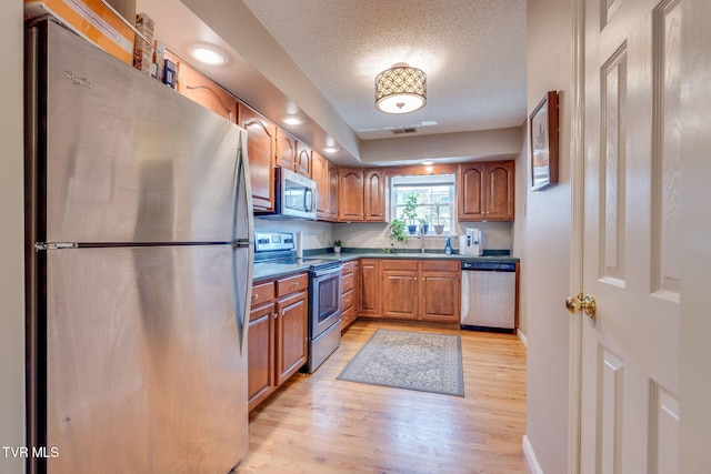 kitchen featuring light wood finished floors, dark countertops, stainless steel appliances, a textured ceiling, and a sink