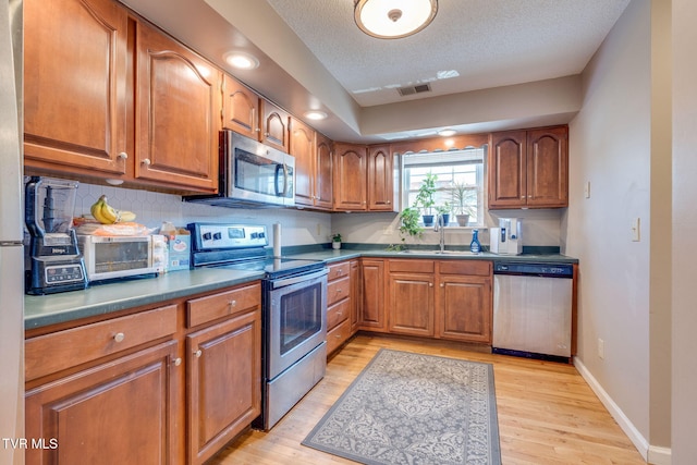 kitchen with a sink, visible vents, appliances with stainless steel finishes, and brown cabinetry