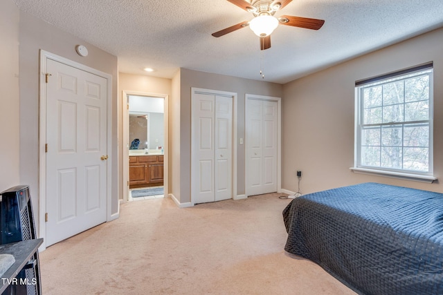 bedroom with two closets, baseboards, light colored carpet, a textured ceiling, and ensuite bath