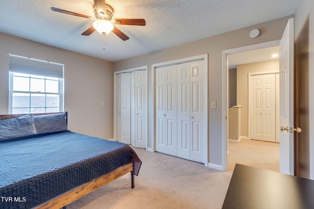 bedroom with light carpet, multiple closets, a ceiling fan, a textured ceiling, and baseboards