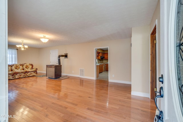 living room featuring baseboards, visible vents, a textured ceiling, a notable chandelier, and light wood-type flooring