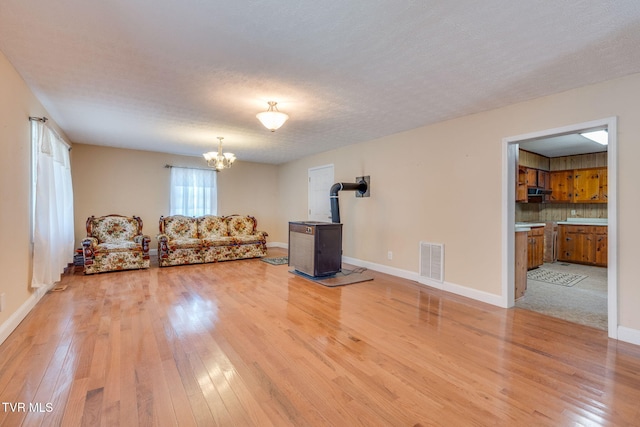 unfurnished living room featuring baseboards, visible vents, light wood finished floors, a wood stove, and a chandelier