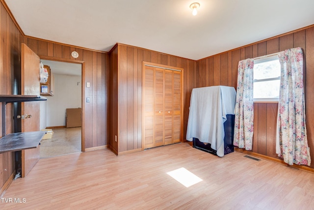 bedroom featuring light wood-type flooring, visible vents, wooden walls, and a closet