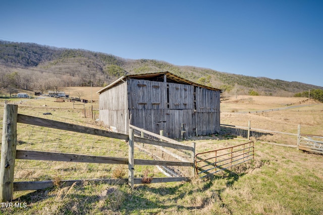 view of outbuilding with a mountain view, a rural view, an outdoor structure, and fence