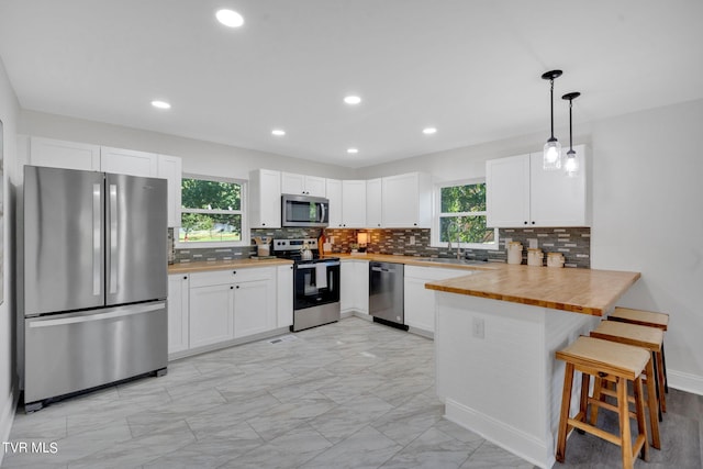 kitchen with a healthy amount of sunlight, appliances with stainless steel finishes, a peninsula, white cabinetry, and a sink