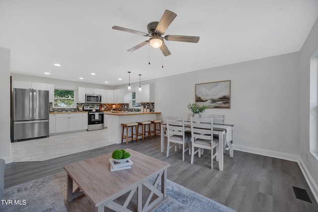 living room featuring a ceiling fan, visible vents, baseboards, light wood finished floors, and recessed lighting