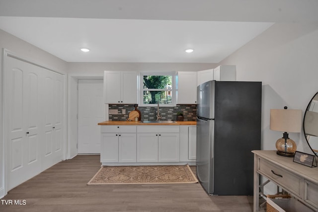 kitchen with light wood finished floors, butcher block counters, decorative backsplash, freestanding refrigerator, and a sink