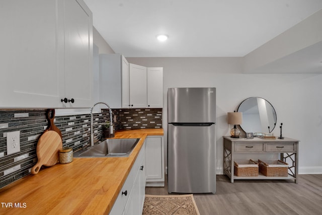 kitchen featuring light wood-style flooring, freestanding refrigerator, a sink, butcher block countertops, and backsplash