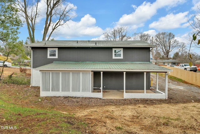 rear view of house with metal roof, fence, brick siding, and a sunroom