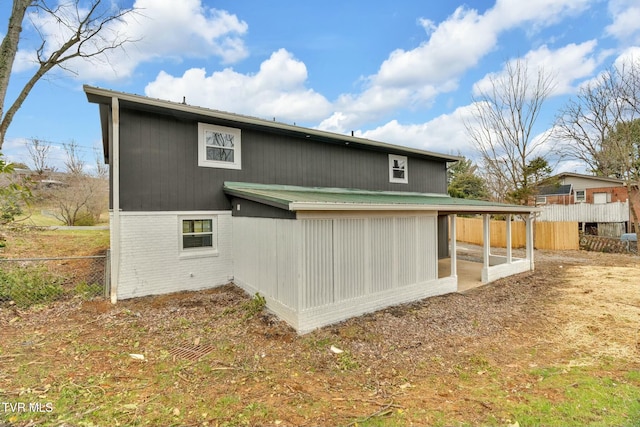 back of property featuring a carport, fence, a sunroom, metal roof, and brick siding