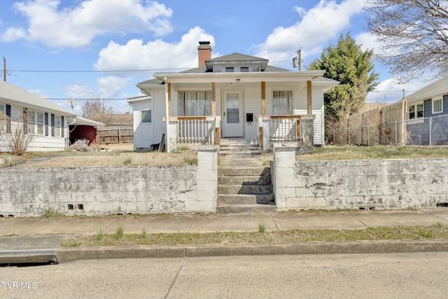 bungalow-style house with covered porch, a chimney, and fence