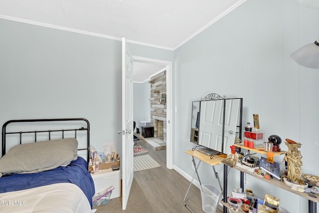 bedroom with a fireplace, crown molding, baseboards, and wood finished floors