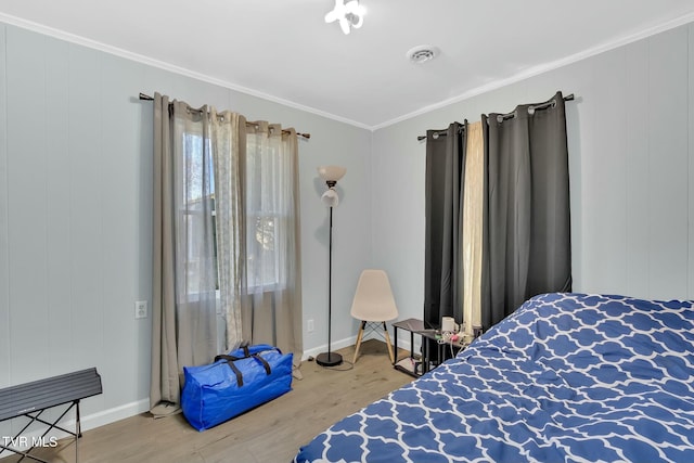 bedroom featuring baseboards, wood finished floors, visible vents, and ornamental molding