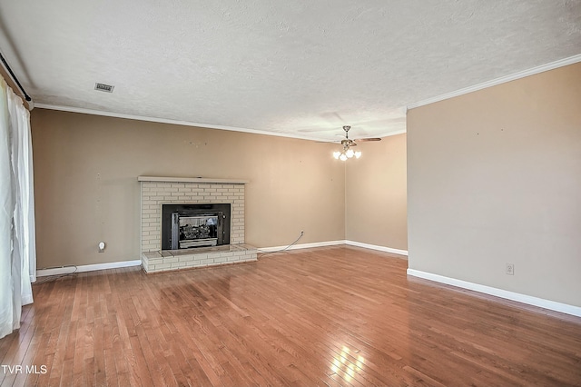 unfurnished living room featuring visible vents, hardwood / wood-style flooring, a textured ceiling, crown molding, and a brick fireplace