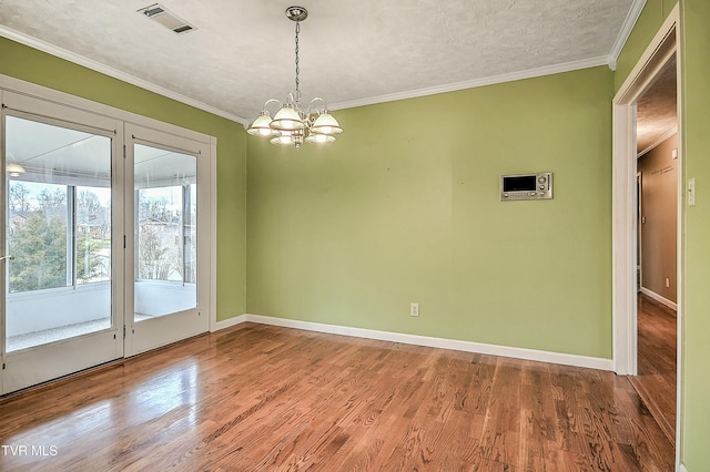 spare room with visible vents, ornamental molding, wood finished floors, an inviting chandelier, and baseboards