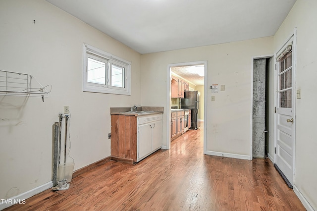 kitchen featuring baseboards, light wood finished floors, freestanding refrigerator, a sink, and light countertops