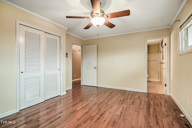 unfurnished bedroom featuring a closet, crown molding, baseboards, and wood finished floors