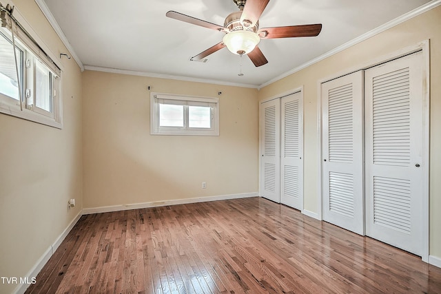 unfurnished bedroom featuring two closets, ceiling fan, baseboards, ornamental molding, and wood-type flooring