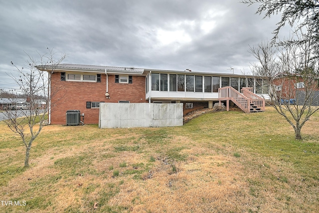 rear view of house with brick siding, stairway, central AC unit, a lawn, and a sunroom